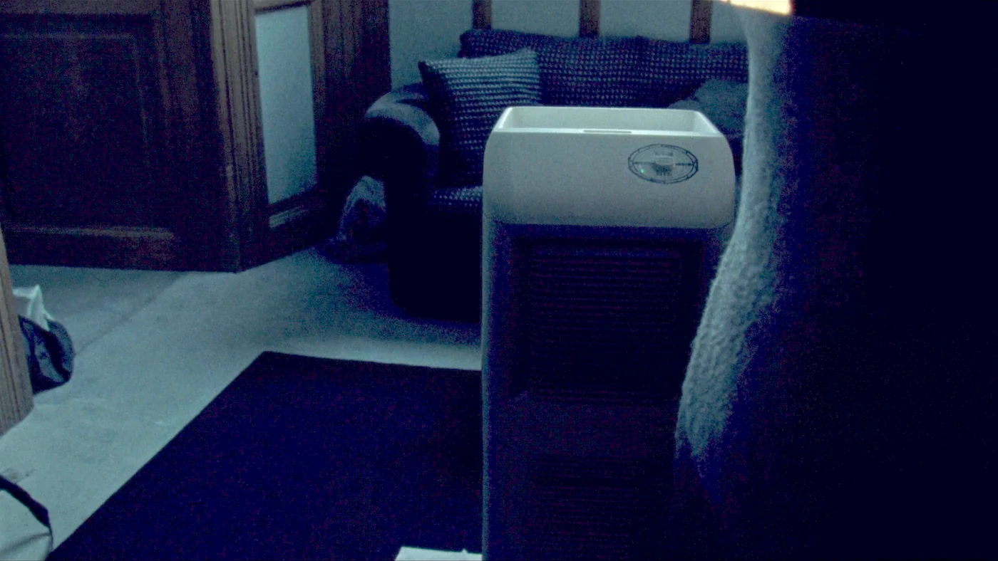 A dehumidifier running quietly beside a sofa in a tenant's living room in the evening
