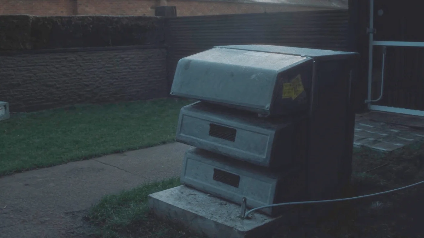 An air source heat pump unit standing on a concrete plinth beside a housing block