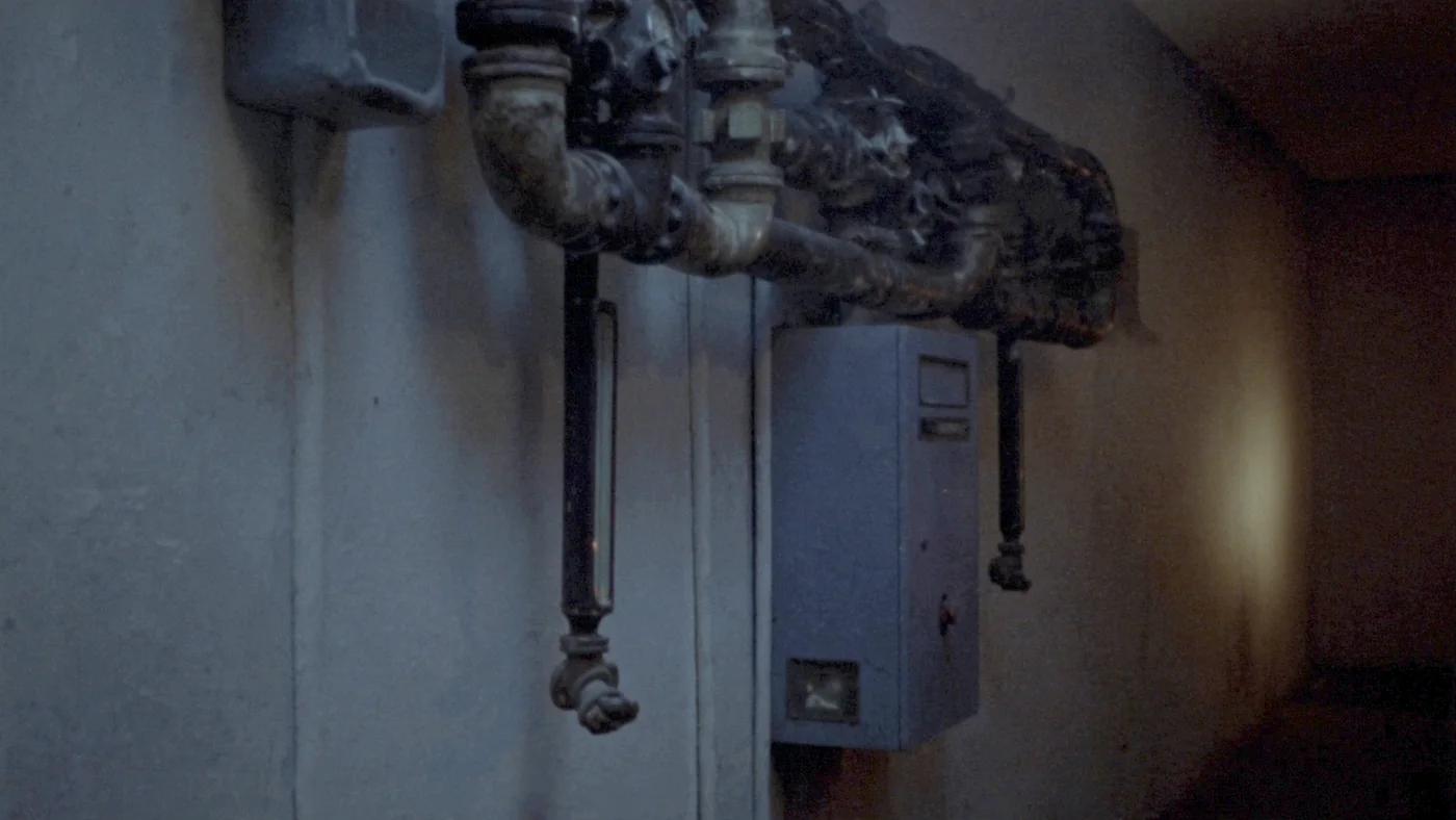 A school boiler room of old pipework and a wall-mounted controller