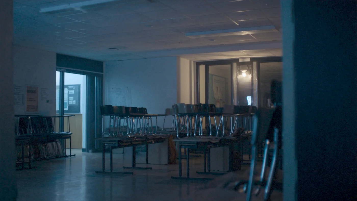 An empty secondary school classroom in low evening light, chairs stacked on desks