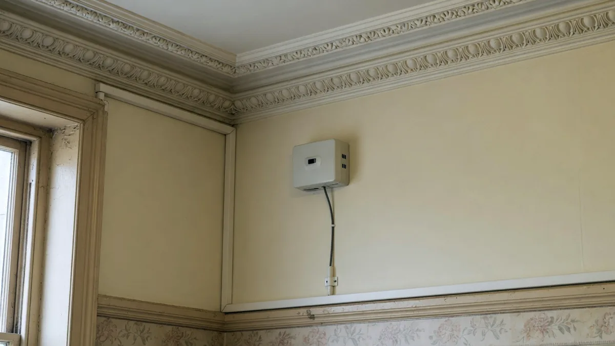 A small modern sensor fitted to the wall of a room with an ornate Victorian cornice