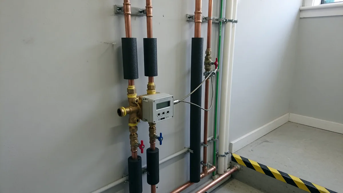 A heat meter fitted into flow and return pipework in a building services riser